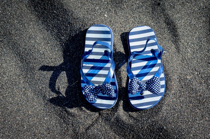 Blue striped flip-flops with bows on sand