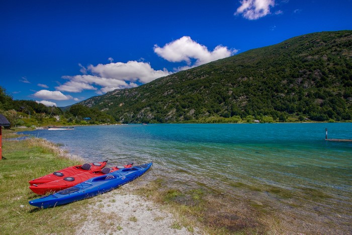 Two kayaks on a sandy shore next to a turquoise lake and forested mountain