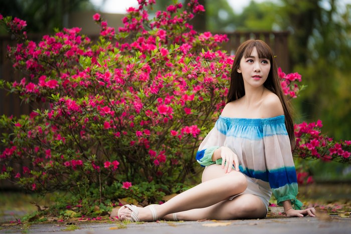 Asian woman with brown hair sitting by pink flowers