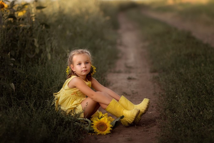 Girl in yellow dress and boots sitting by a dirt path