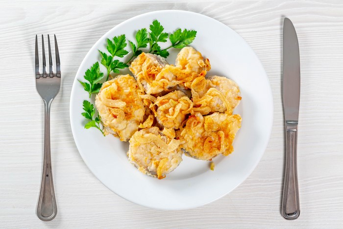 Fried fish pieces with fried onions on a plate with fork and knife