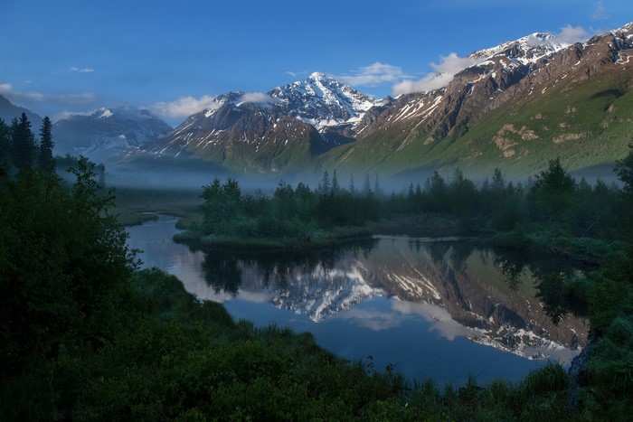 Snow-capped mountains reflected in a calm river in Alaska