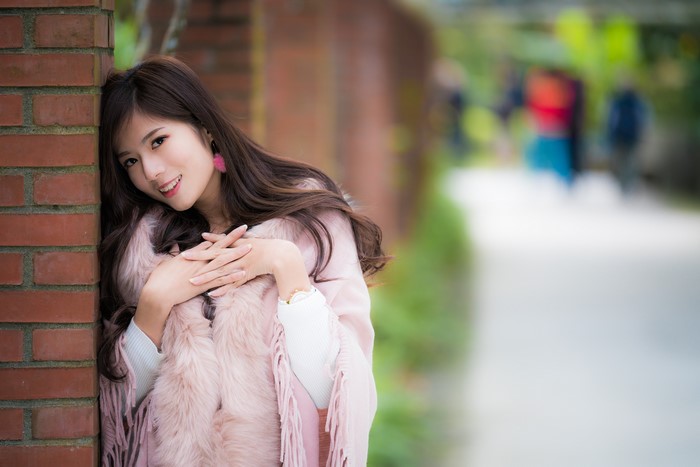 Asian woman in pink fur coat posing by brick wall