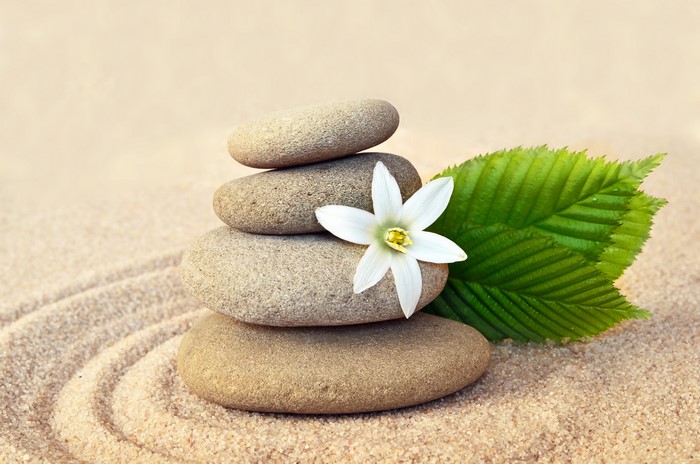 Zen stones stacked on sand with a flower and leaf