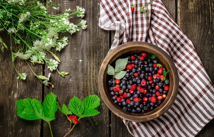 Bowl of berries with wildflowers and leaves on wood