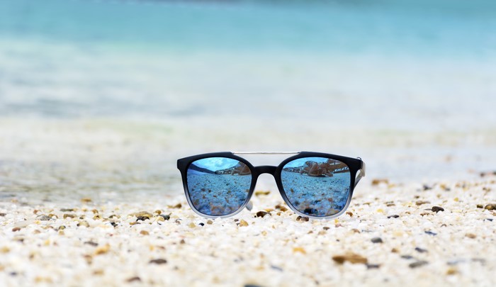 Sunglasses on a pebble beach with ocean reflection