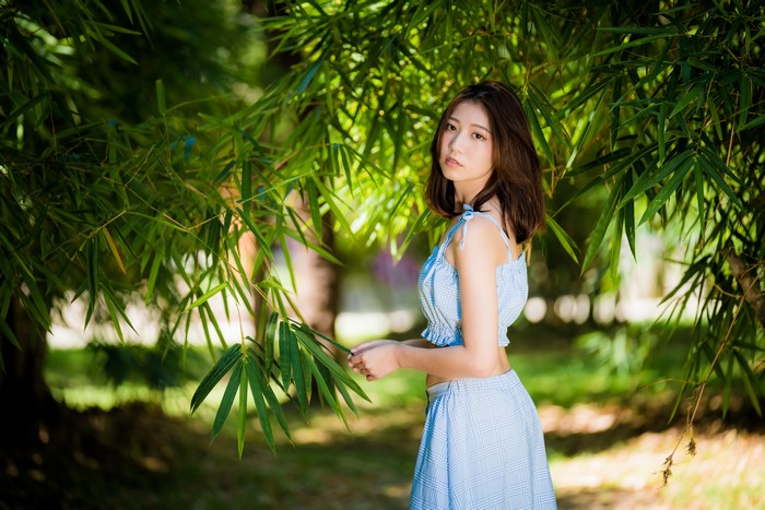 Asian girl with brown hair in a blue outfit near bamboo