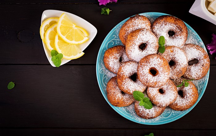 Donuts with powdered sugar, lemons, and mint on a plate