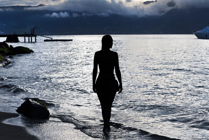 Silhouette of a woman walking into the sea at sunset