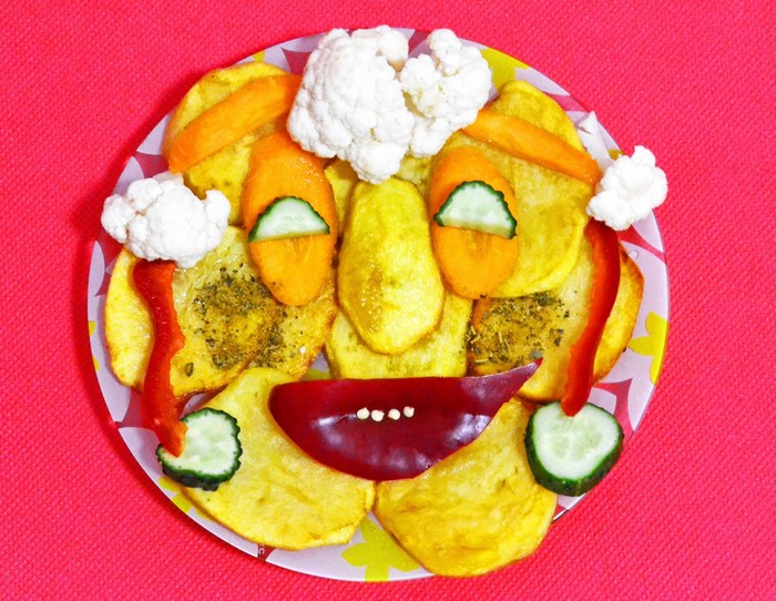 Creative face made of potatoes and vegetables on a pink background