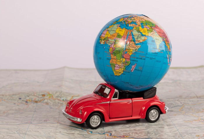 Red toy convertible car carrying a globe on a map