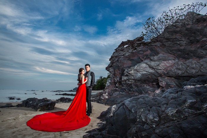 Couple in Red Dress and Suit on Beach with Rocks