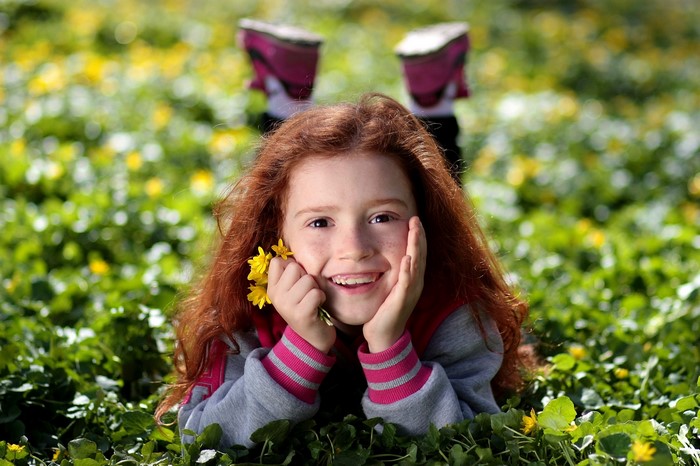 Redhead girl lying in grass with yellow flowers