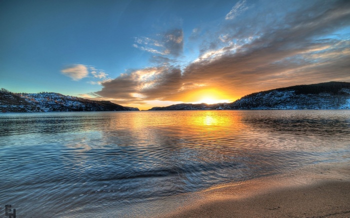 Sunset over a calm bay with snow-covered hills