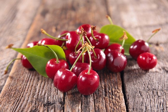 Cherries with leaves on wooden surface