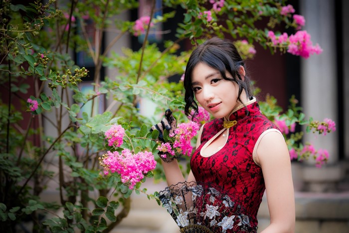 Asian woman in red dress with hand fan and pink flowers