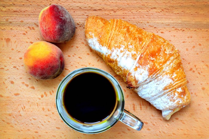 Coffee, Croissant, and Peaches on a Wooden Surface