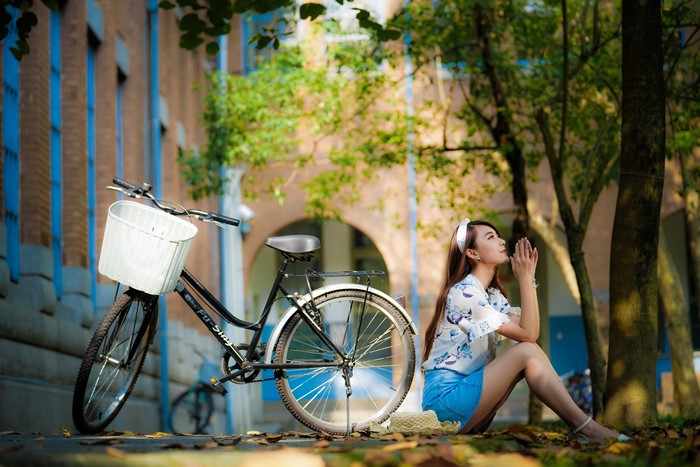 Asian woman sitting by a bicycle with a wicker basket