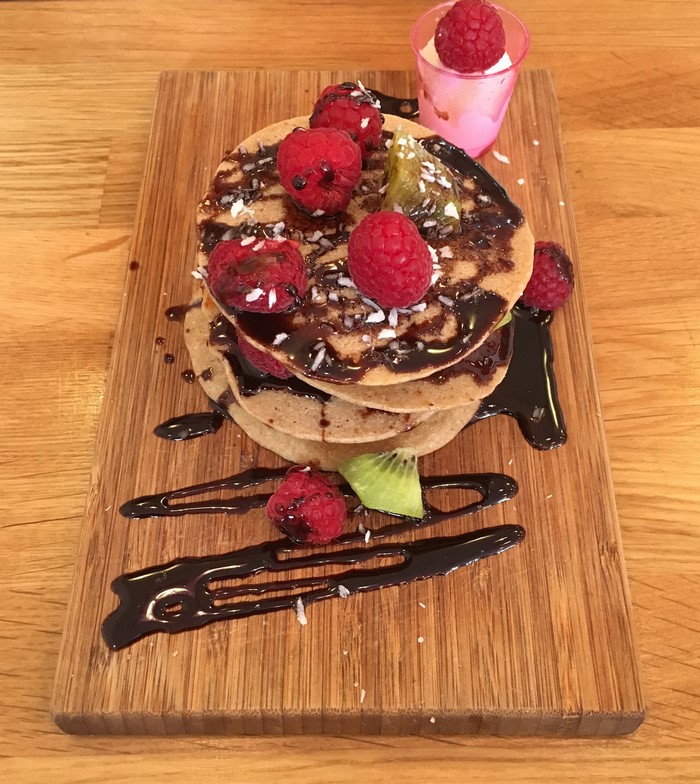 Pancakes with raspberries, kiwi, chocolate sauce, and coconut flakes on a cutting board