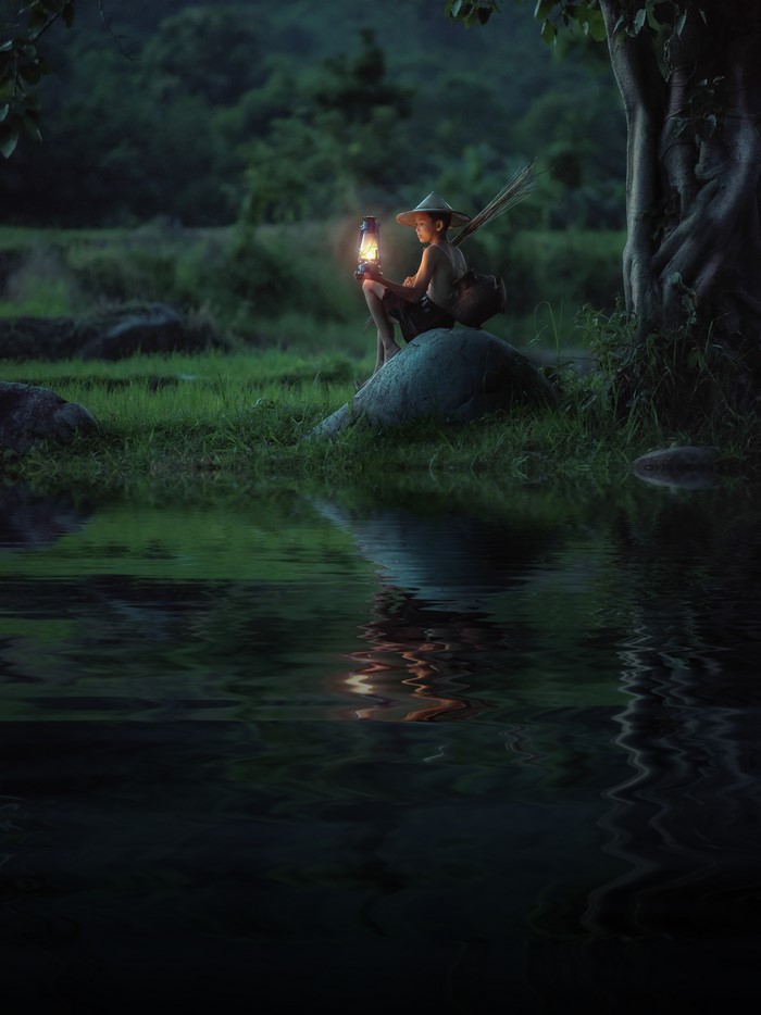 Boy with kerosene lamp sitting on a stone at night