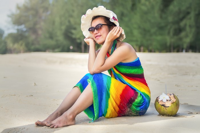 Asian woman in hat and sarong on beach with coconut
