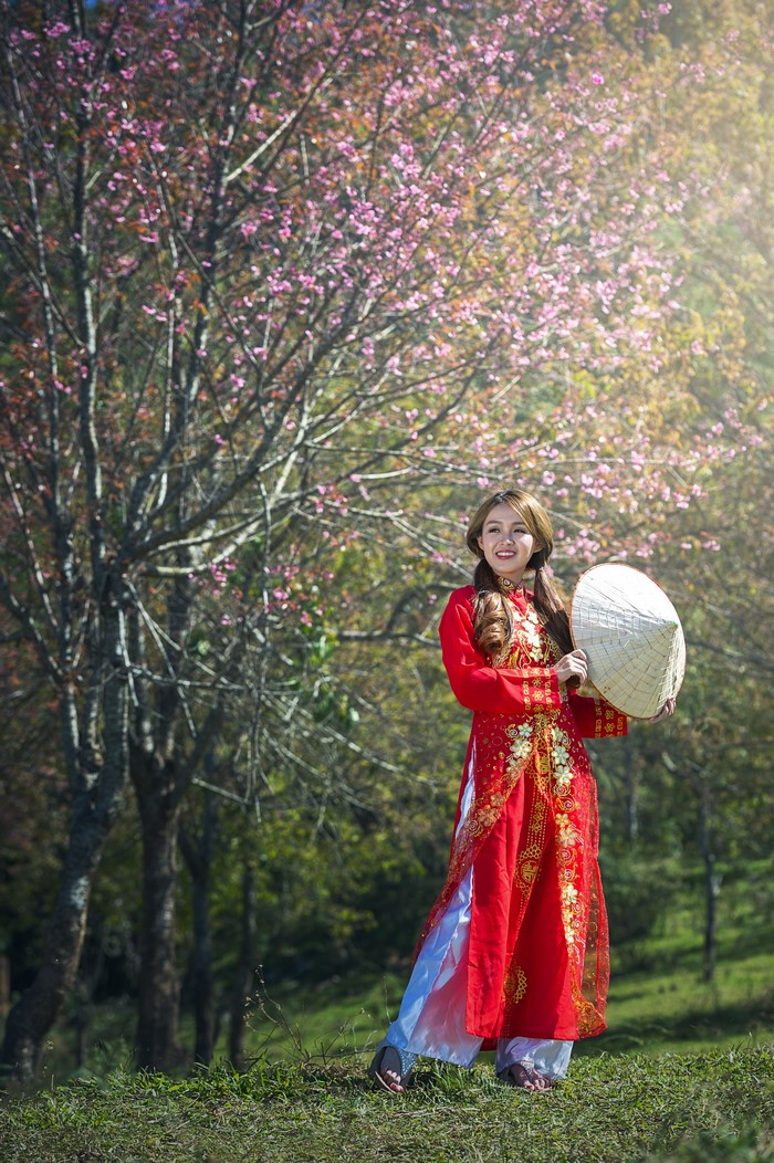 Woman in red dress holding a conical hat near flowering trees