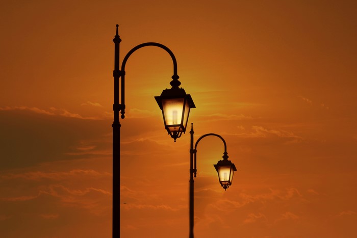 Two street lights against an orange sunset sky