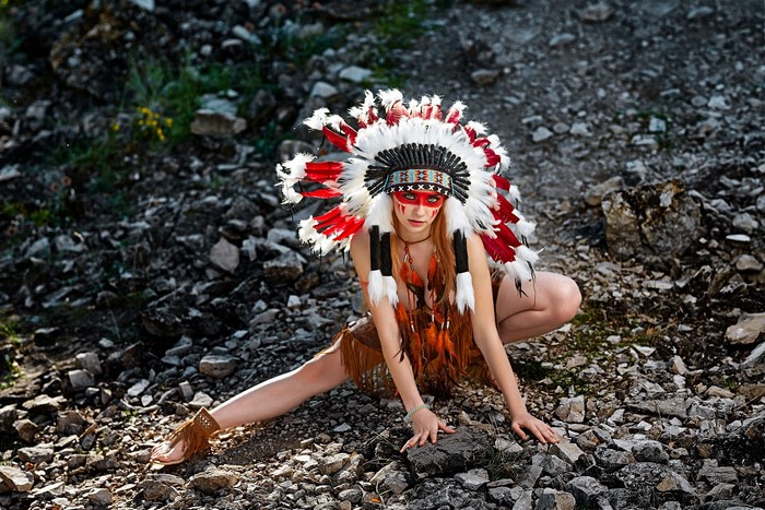 Woman Wearing Red and White War Bonnet on Rocky Ground
