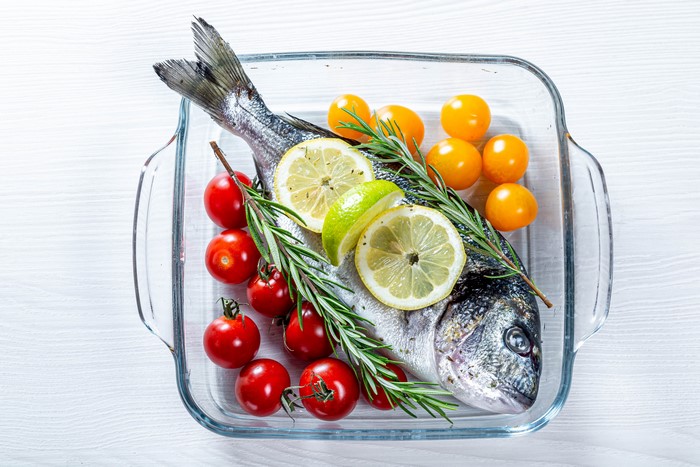 Whole fish with tomatoes, lemon, and rosemary in baking dish