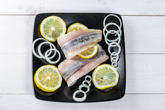 Herring fillets with lemon and onion rings on a black plate