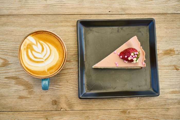 Cappuccino and strawberry cake slice on wooden table
