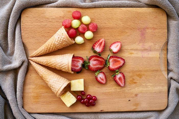 Ice cream cones with strawberries, melon, and pineapple on a cutting board