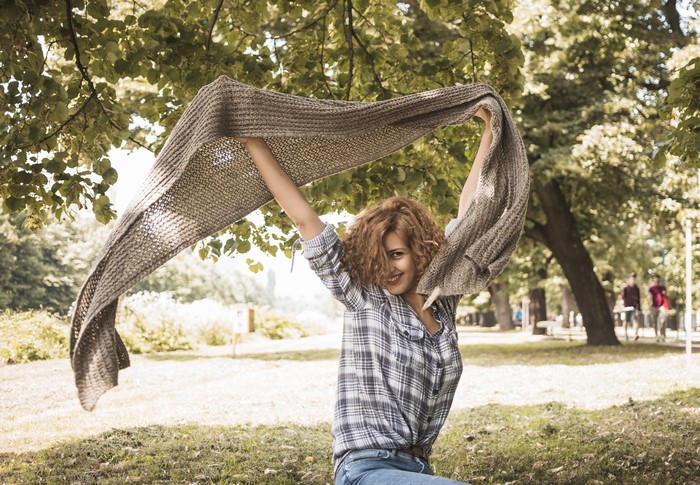 Woman with red hair holding a scarf in a park