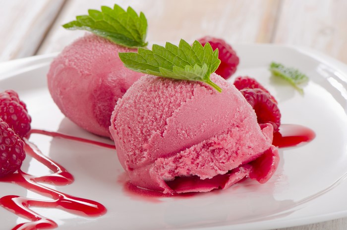 Two scoops of raspberry ice cream with raspberries and mint