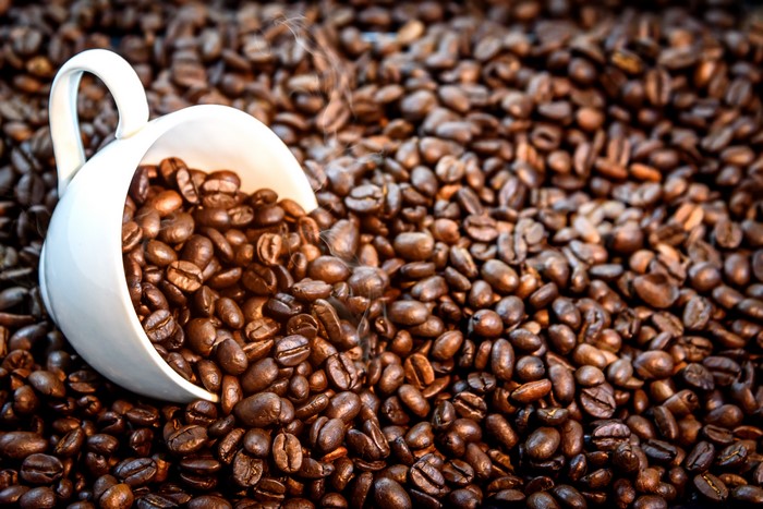 White cup spilling coffee beans on a bed of coffee beans