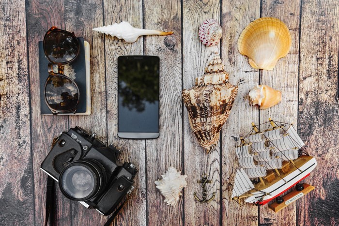 Travel items on wooden background: camera, phone, sunglasses, shells, ship