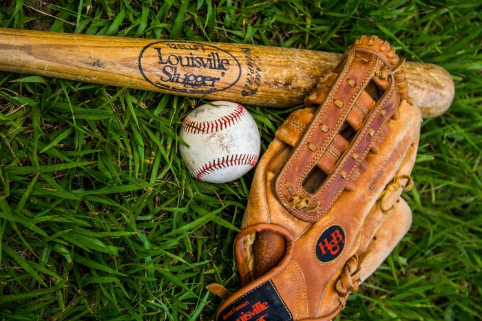 Louisville Slugger baseball bat, ball, and glove on grass