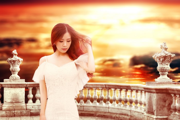 Asian woman in white dress on balcony at sunset