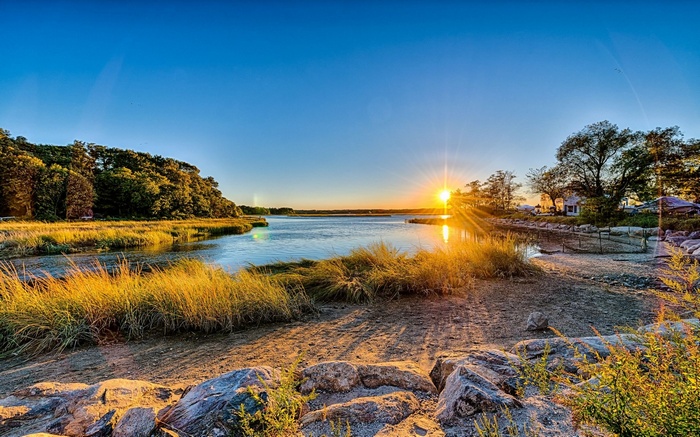 Sunset over a marshy coastline with trees and houses