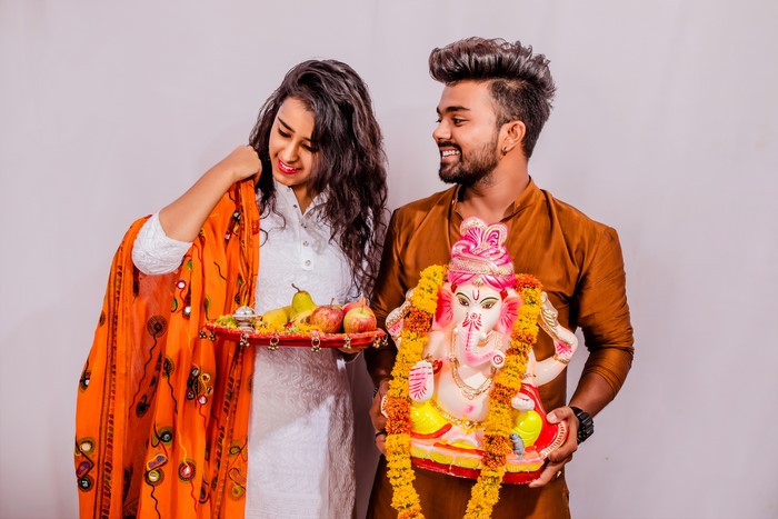 Couple celebrating Ganesh Chaturthi with idol and fruits
