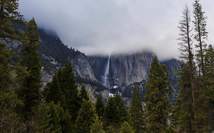 Waterfall cascading down a rocky mountain shrouded in clouds