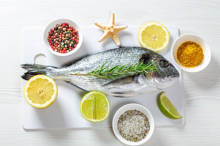 Raw fish with lemon, lime, spices, and rosemary on a cutting board