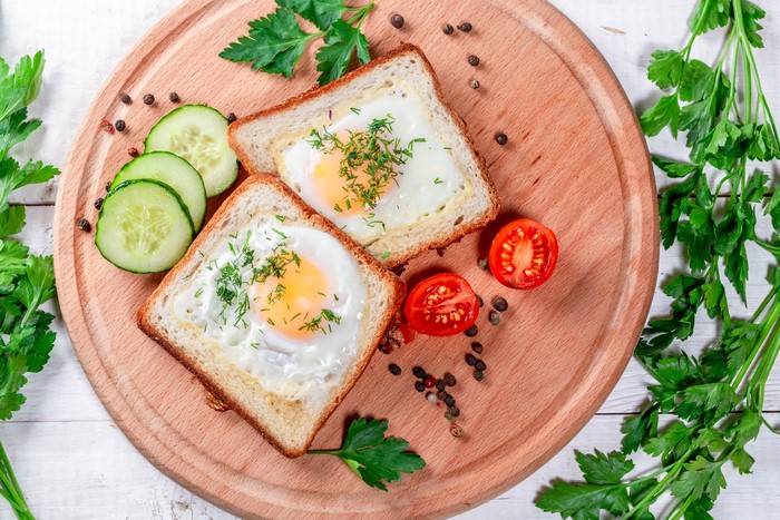 Two eggs in toast with tomatoes and cucumbers on a cutting board