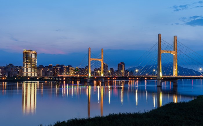 Cable-stayed bridge over a river at dusk with city skyline