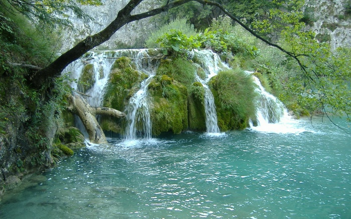 Turquoise water flows over moss-covered rocks in a waterfall
