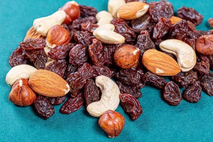 Mixed nuts and raisins on a teal background