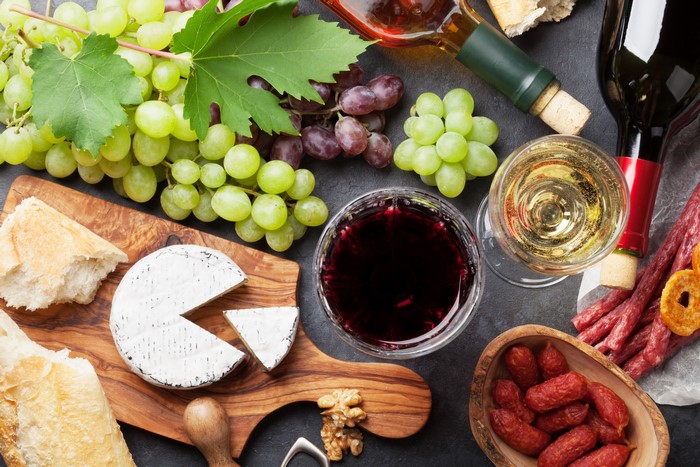Wine, Grapes, Cheese, Sausage, and Bread on a Cutting Board