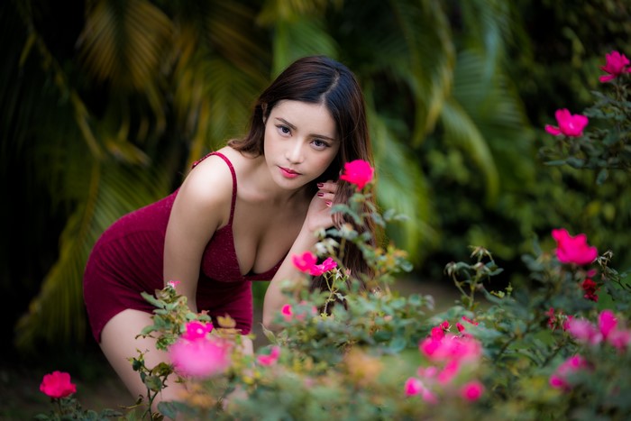 Asian woman in red dress posing near pink roses