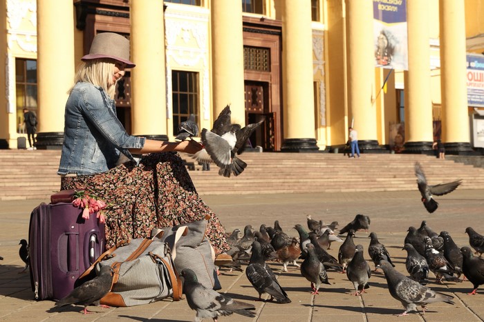 Blonde girl in hat feeding pigeons with luggage