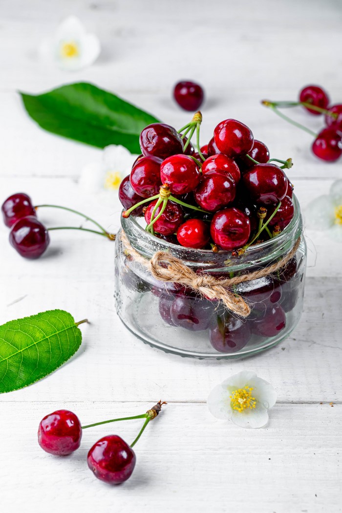 Cherries in a glass jar with flowers and leaves